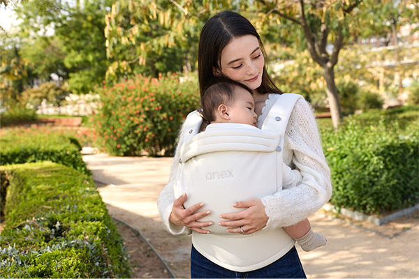 Ergonomiczne nosidełko Anex Whiz Hug ecru – mama niesie niemowlę przodem do siebie