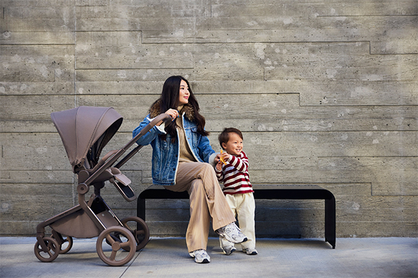 Mama z dzieckiem podczas spaceru z wózkiem Anex Flo – brązowy, lekki wózek 2w1 z siedziskiem spacerowym, idealny do miejskich spacerów i codziennego użytkowania.