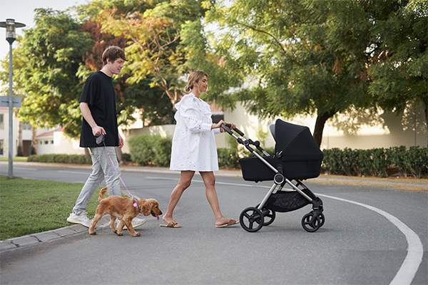 Para spacerująca z wózkiem Anex iQ w miejskim otoczeniu – elegancki, czarny wózek dziecięcy z gondolą na lekkim stelażu, idealny do codziennych spacerów po mieście.