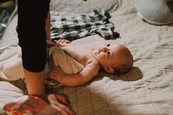Przewijanie niemowlęcia na łóżku, codzienna pielęgnacja dziecka w trakcie skoku rozwojowego
