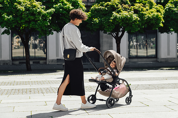 Kobieta prowadzi wózek spacerowy Britax Römer RIO z dzieckiem podczas spaceru w mieście.