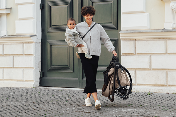Kobieta swobodnie niesie lekki, składany wózek Britax Römer RIO w jednej ręce.